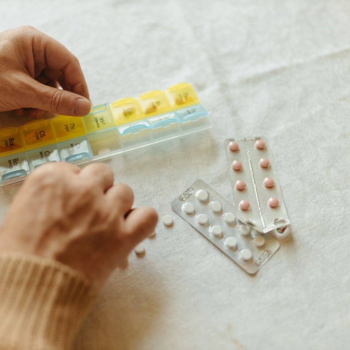 Manos organizando pastillas en un pastillero semanal